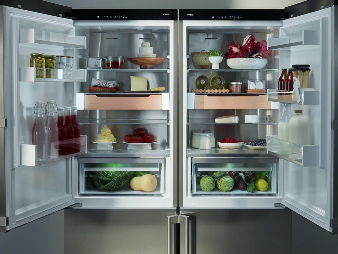 Two open refrigerators in stainless steel with colorful food inside