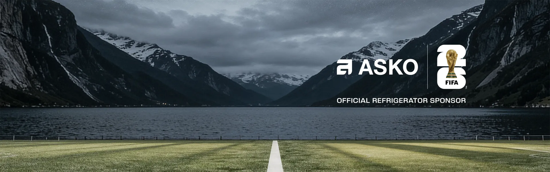 Football field by a fjord with mountains, featuring ASKO and FIFA sponsor logos Football field by a fjord with mountains, featuring ASKO and FIFA sponsor logos