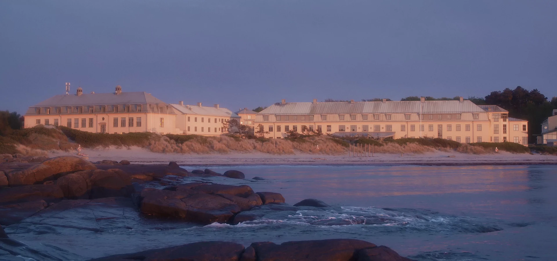 Varberg Kusthotel viewed from the shoreline at sunset, with rocky coastline and calm sea in the foreground. Varberg Kusthotel viewed from the shoreline at sunset, with rocky coastline and calm sea in the foreground.