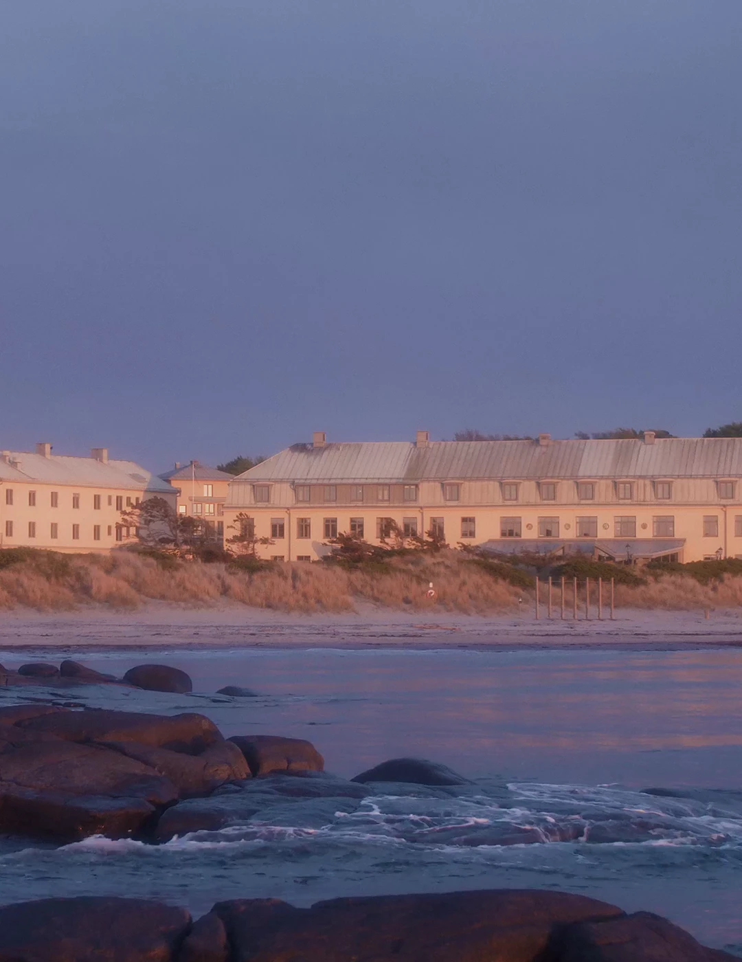 Varberg Kusthotel viewed from the shoreline at sunset, with rocky coastline and calm sea in the foreground. Varberg Kusthotel viewed from the shoreline at sunset, with rocky coastline and calm sea in the foreground.